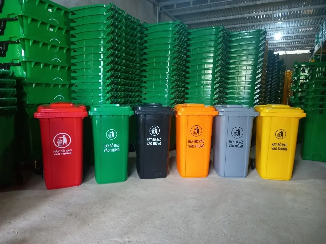 Sáu thùng rác nhựa có bánh xe màu đỏ, xanh, đen, cam, xám và vàng